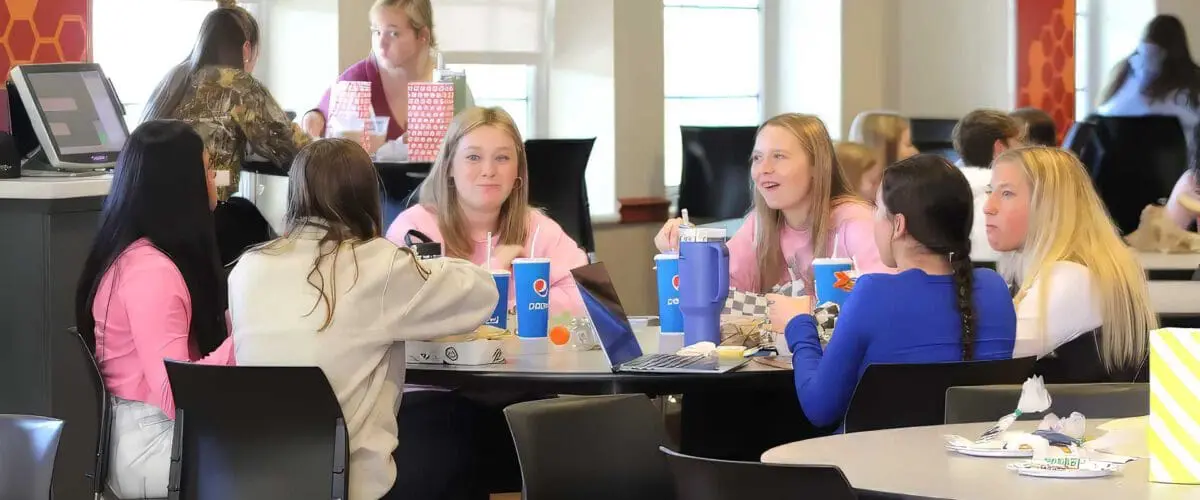 Students sitting around a table in Beehive having conversation and enjoying beverages