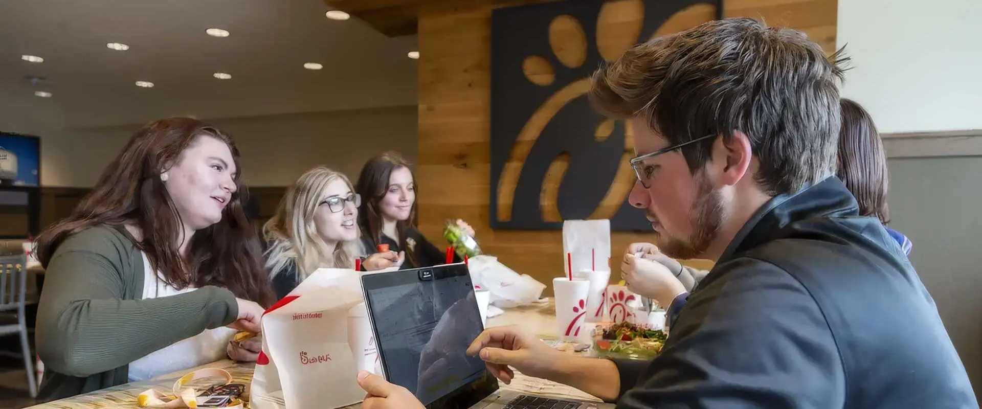 Students having a meal at Chick-fil-A while another works on laptop